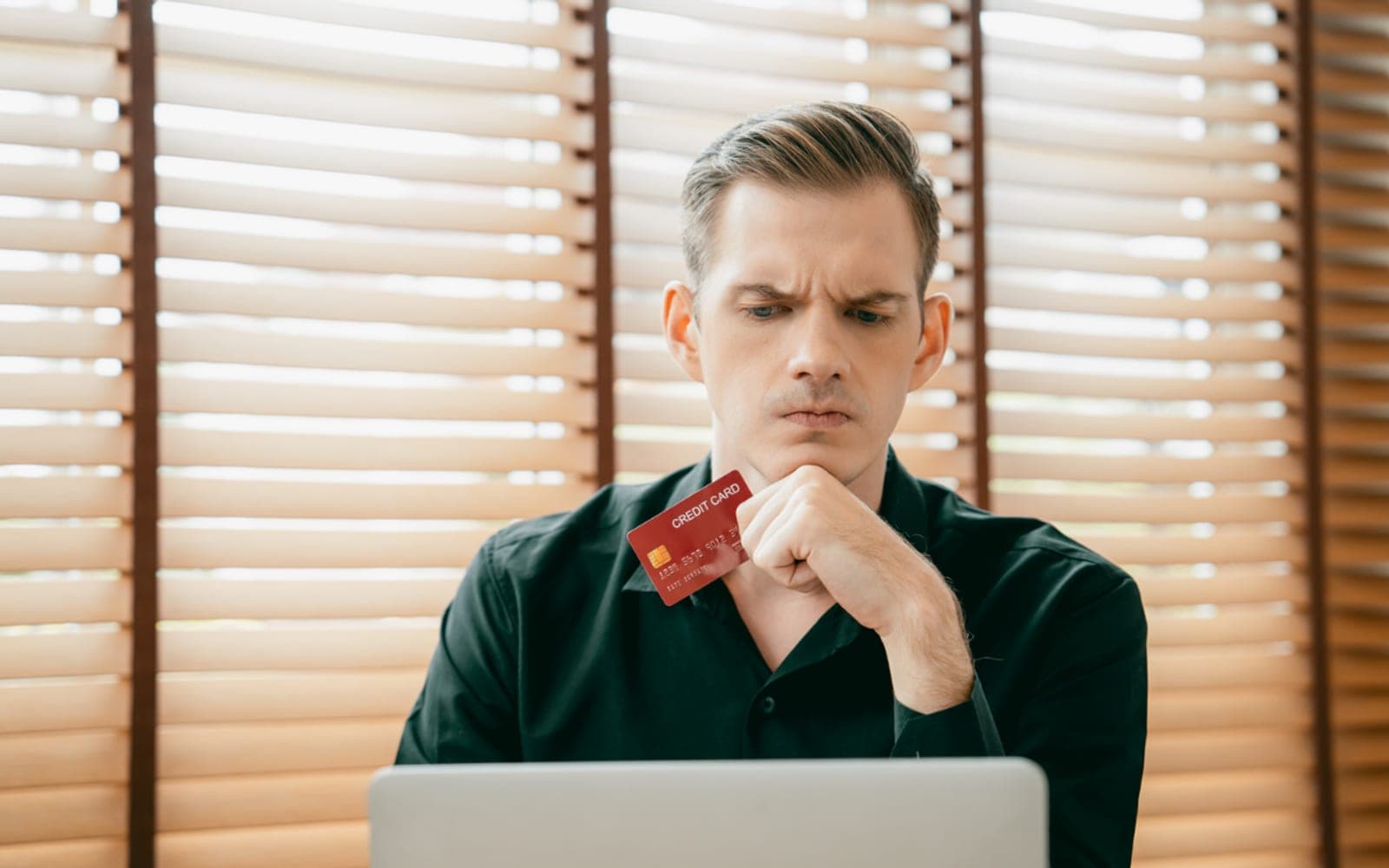 A shopper holding a credit card studies an online shop with a doubtful look